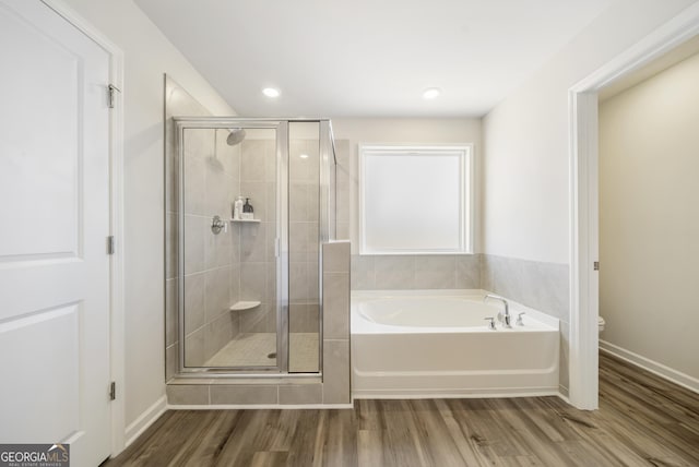 bathroom with baseboards, toilet, a garden tub, a stall shower, and wood finished floors