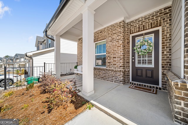 view of exterior entry with brick siding and a porch