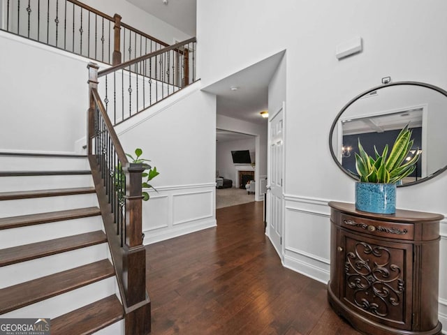 staircase featuring a wainscoted wall, a fireplace, a decorative wall, a towering ceiling, and hardwood / wood-style floors