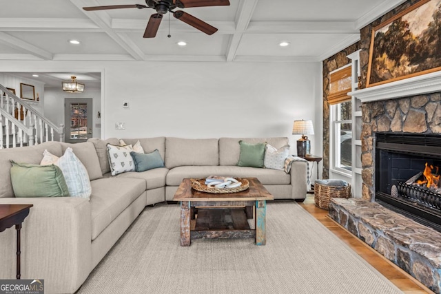 living room featuring coffered ceiling, beamed ceiling, a stone fireplace, and light wood finished floors