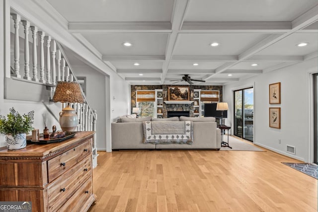 living room with light wood finished floors, visible vents, coffered ceiling, stairway, and a stone fireplace