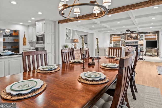 dining space featuring beam ceiling, recessed lighting, light wood-style flooring, a stone fireplace, and coffered ceiling