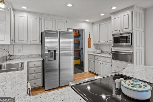 kitchen with appliances with stainless steel finishes, white cabinetry, a sink, and backsplash