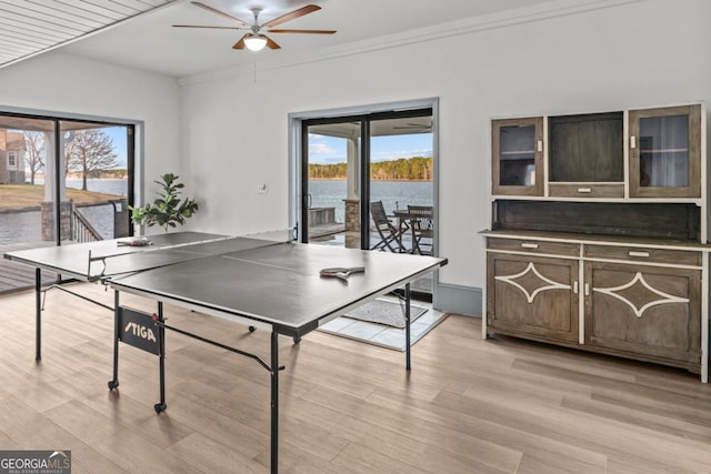 playroom featuring a ceiling fan, a water view, crown molding, and light wood-style flooring