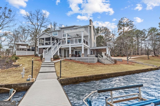 back of property with a water view, a sunroom, a yard, stairway, and a pergola