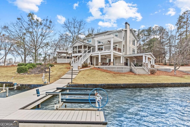 rear view of house featuring a water view, a sunroom, stairs, and a lawn