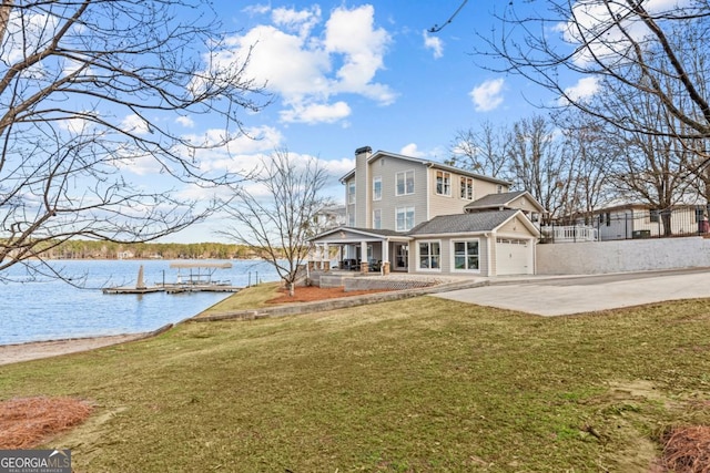 back of property with concrete driveway, a patio, a chimney, a water view, and a yard