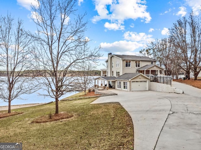 view of front of home with a porch, an attached garage, concrete driveway, a chimney, and a front yard