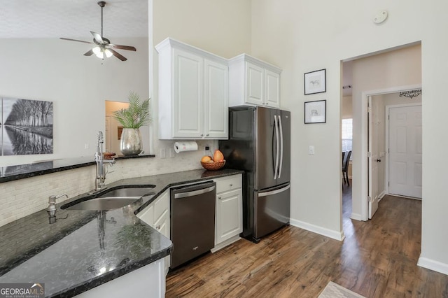 kitchen featuring dark stone counters, dark wood-style floors, stainless steel appliances, white cabinetry, and a sink