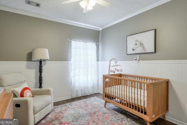 bedroom with a wainscoted wall, crown molding, visible vents, wood finished floors, and a crib