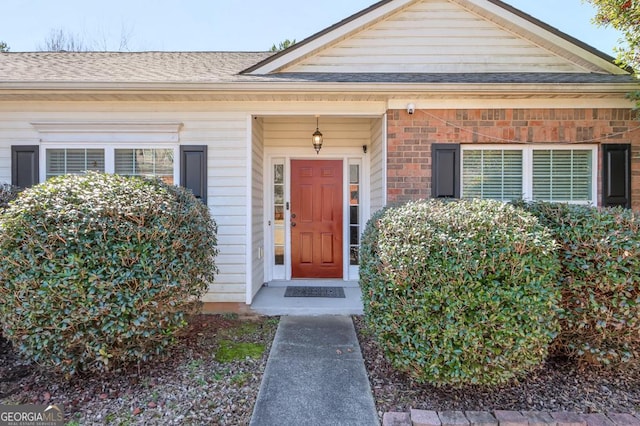 view of exterior entry featuring brick siding and roof with shingles