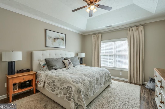 bedroom with dark wood-style flooring, visible vents, baseboards, ornamental molding, and a tray ceiling