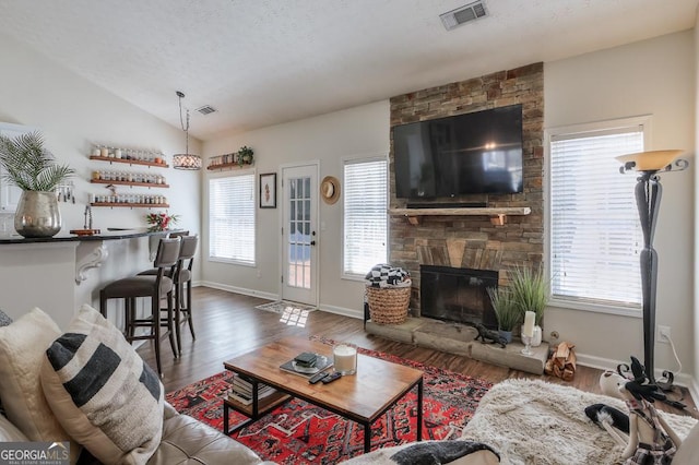 living area featuring a wealth of natural light, vaulted ceiling, visible vents, and a fireplace