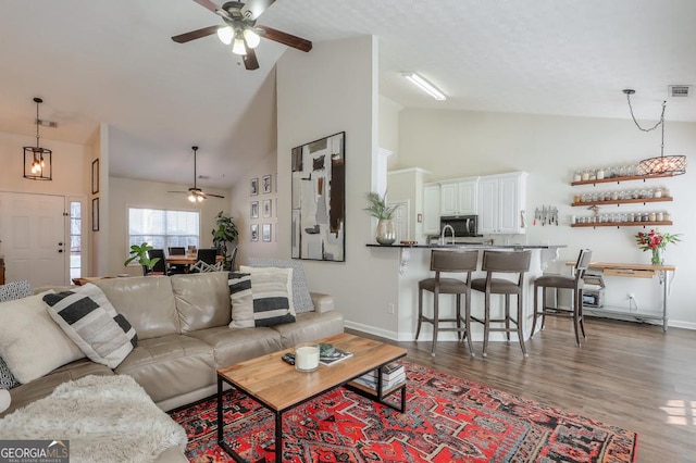 living room with dark wood-style flooring, visible vents, a ceiling fan, high vaulted ceiling, and baseboards