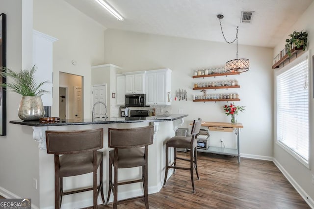 kitchen with dark countertops, black microwave, white cabinetry, and a peninsula