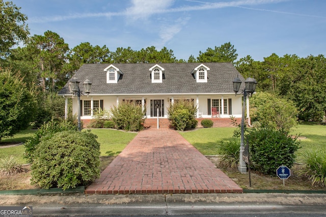 cape cod-style house featuring a shingled roof and a front yard