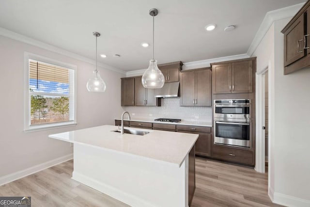 kitchen featuring a kitchen island with sink, light countertops, under cabinet range hood, double oven, and a sink