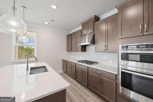 kitchen with under cabinet range hood, stainless steel appliances, a sink, light countertops, and decorative light fixtures