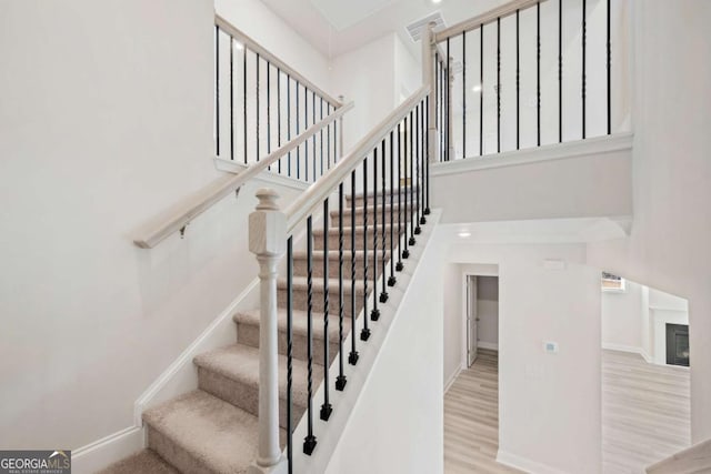 stairs with a glass covered fireplace, a towering ceiling, baseboards, and wood finished floors