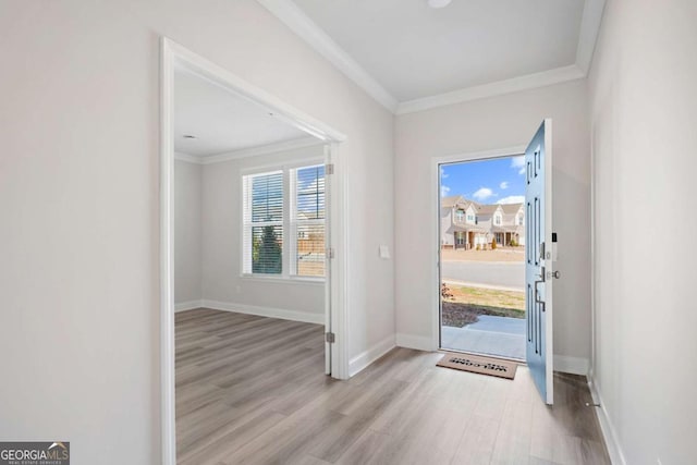 entryway with light wood-style flooring, ornamental molding, and baseboards