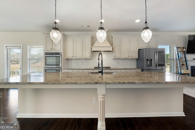 kitchen featuring light stone counters, visible vents, appliances with stainless steel finishes, a large island with sink, and pendant lighting