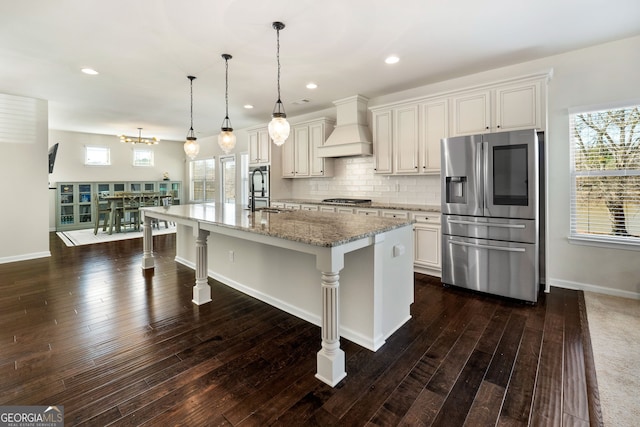 kitchen featuring a breakfast bar area, appliances with stainless steel finishes, white cabinets, an island with sink, and premium range hood