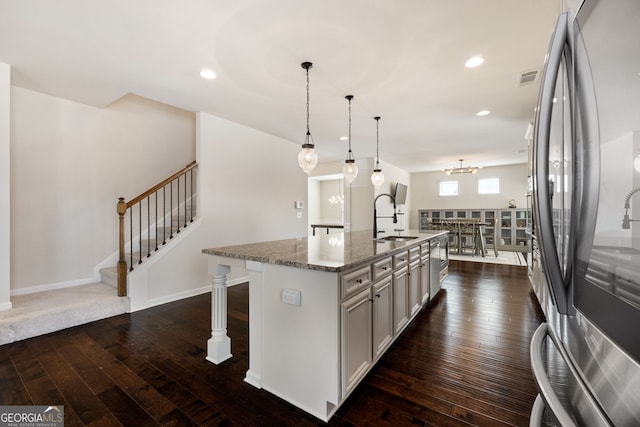 kitchen featuring stone countertops, an island with sink, stainless steel refrigerator, hanging light fixtures, and a sink