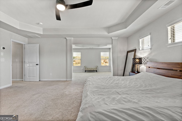 bedroom featuring light carpet, a tray ceiling, multiple windows, and baseboards