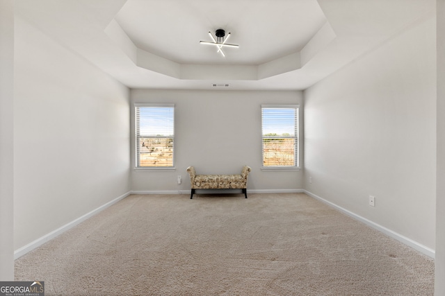 unfurnished room with a tray ceiling, light carpet, visible vents, and baseboards