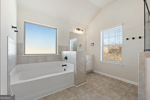 bathroom featuring lofted ceiling, a garden tub, baseboards, and vanity