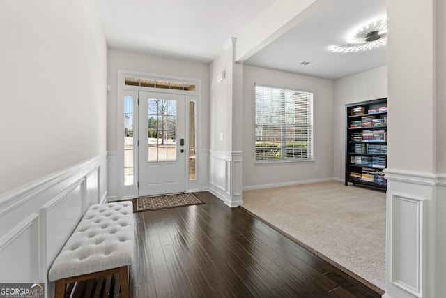 carpeted entrance foyer with plenty of natural light, a decorative wall, wood finished floors, and wainscoting