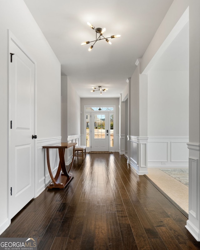 entryway featuring dark wood-style flooring, a decorative wall, ornate columns, and an inviting chandelier