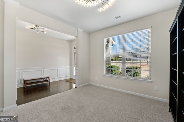 empty room featuring a decorative wall, dark carpet, visible vents, and a notable chandelier