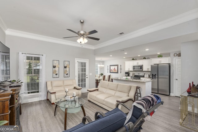 living area with ceiling fan with notable chandelier, ornamental molding, light wood-type flooring, and visible vents