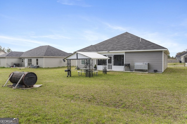 rear view of house featuring a gazebo, a lawn, and roof with shingles