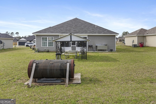 rear view of house featuring roof with shingles, a lawn, and central AC unit