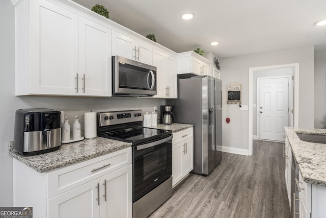 kitchen featuring stainless steel appliances, white cabinets, and light stone countertops
