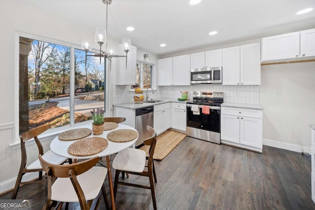 kitchen with light stone counters, stainless steel appliances, a sink, white cabinets, and pendant lighting