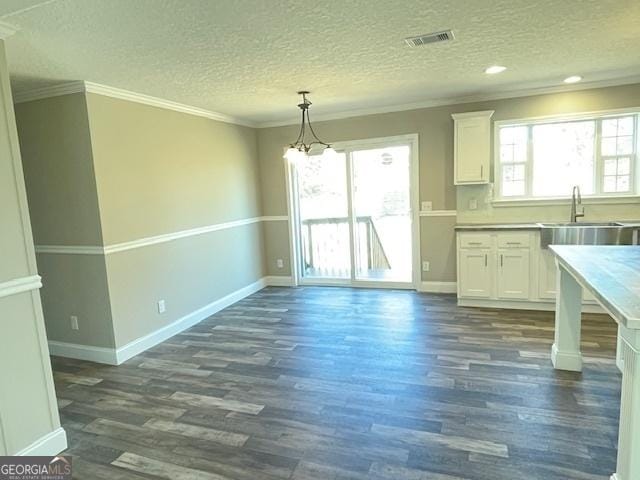 unfurnished dining area with a sink, visible vents, baseboards, ornamental molding, and dark wood finished floors