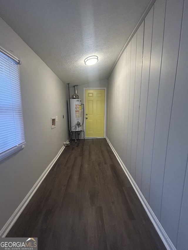 hallway featuring water heater, a textured ceiling, dark wood finished floors, and baseboards