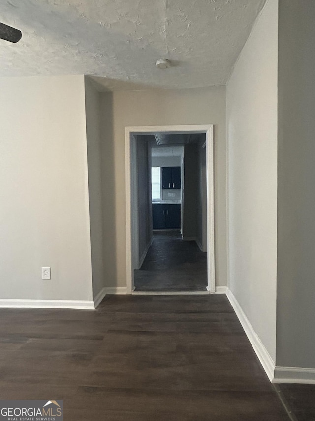 hall featuring a textured ceiling, baseboards, and dark wood-type flooring