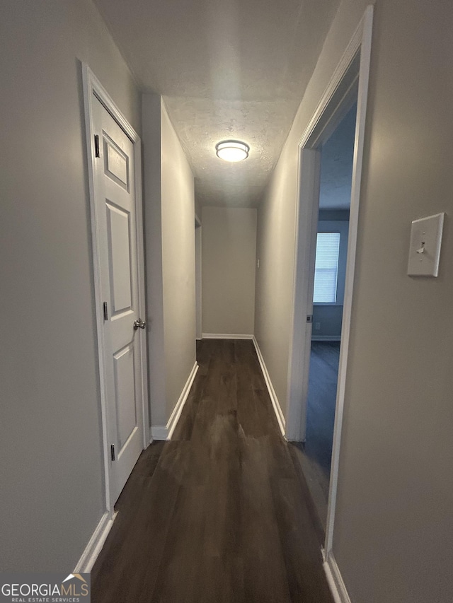 hallway with dark wood-type flooring, a textured ceiling, and baseboards