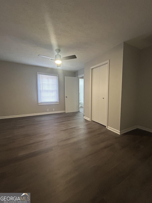 unfurnished bedroom with a ceiling fan, a textured ceiling, baseboards, and dark wood-style flooring