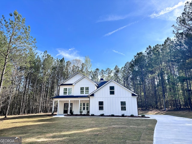 modern farmhouse style home with a porch, board and batten siding, a front yard, and a wooded view