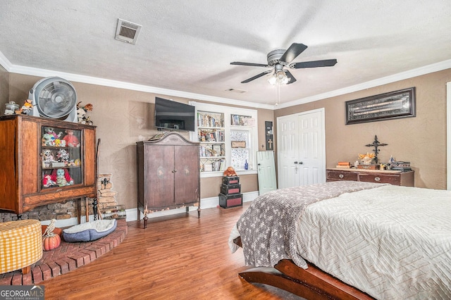 bedroom with ornamental molding, wood finished floors, visible vents, and a textured ceiling