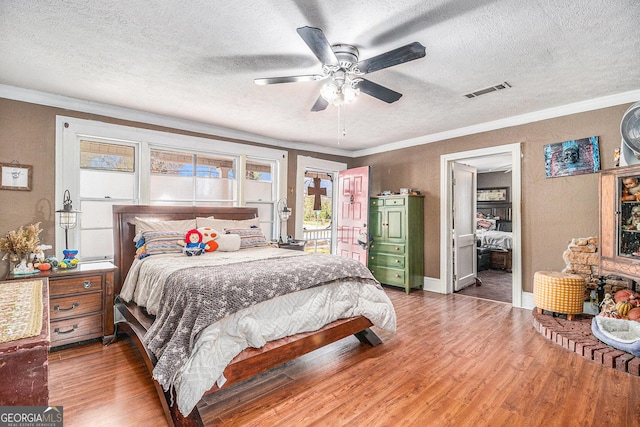 bedroom with visible vents, ornamental molding, wood finished floors, a textured ceiling, and a ceiling fan