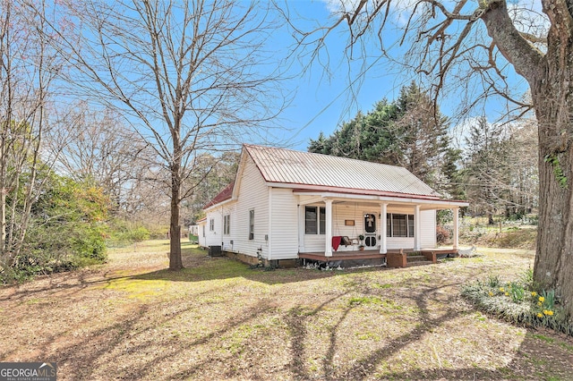 view of front of home with metal roof, central air condition unit, covered porch, and a front yard