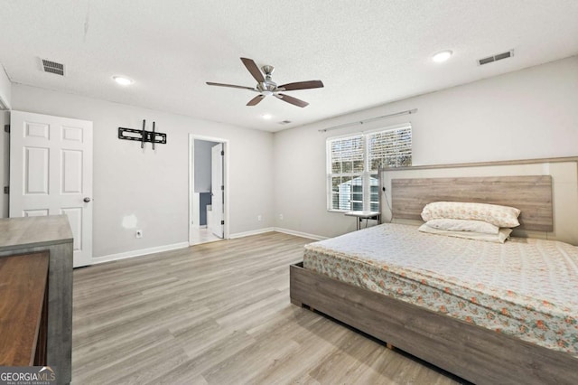 bedroom with a textured ceiling, wood finished floors, visible vents, and baseboards