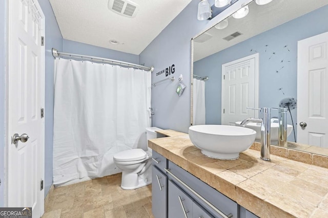 bathroom with toilet, stone finish flooring, visible vents, and vanity