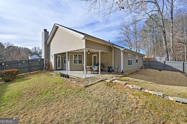 rear view of property featuring a ceiling fan, a fenced backyard, a chimney, a yard, and a patio area